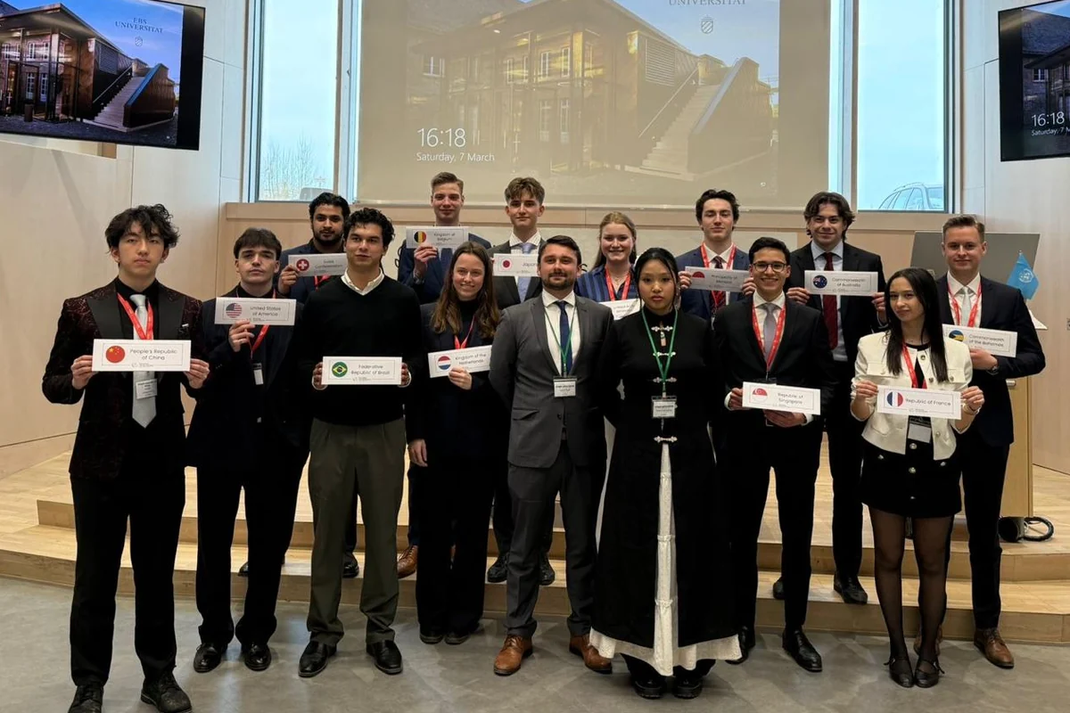 Delegates of the first EBSMUN on stage in the EBS lecture hall, each holding their country placard